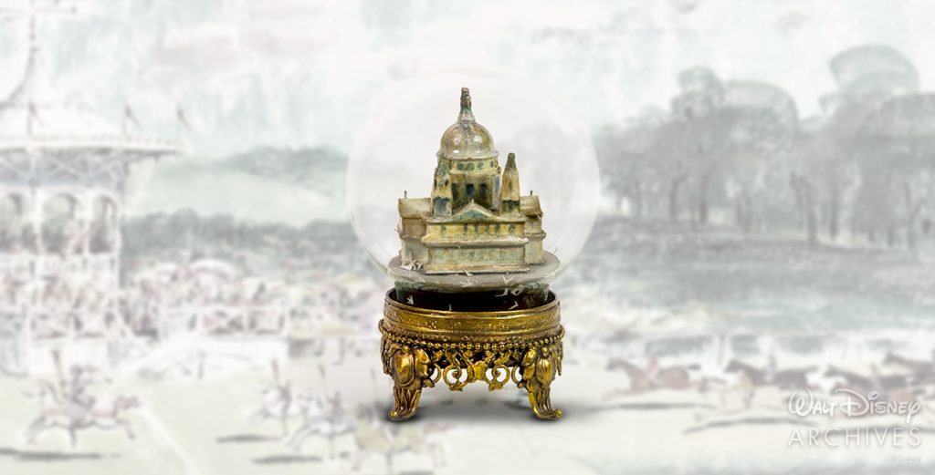 Shown is a snow globe prop featuring St. Paul’s Cathedral. The globe has been drained of water and features a painted cathedral within a circular dome. There are paper birds at the bottom of the globe, which has an intricate golden metal base.