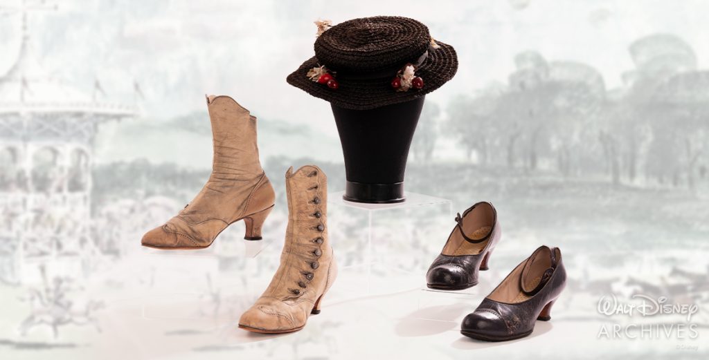 Several pieces of Mary Poppins’ wardrobe, all worn by Disney Legend Julie Andrews are shown. From left, the items include Mary’s since-painted-white “Jolly Holiday” boots with silver metal buttons, her Edwardian-style black straw hat with faux red cherries and white silk daisies, and her blue leather shoes on the right.