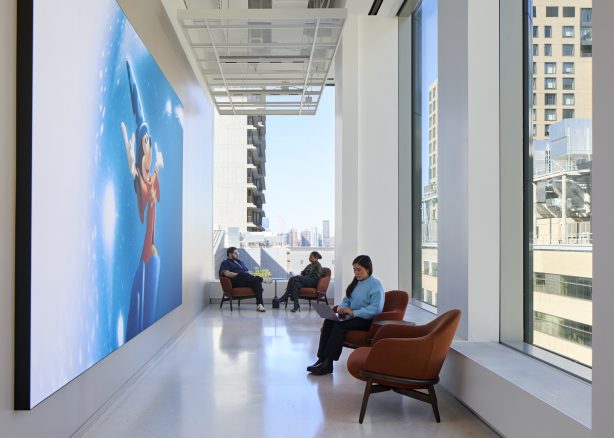 Employees sitting in a collaborative space with Disney artwork on the wall by Dave Burk – SOM © 2024 Disney